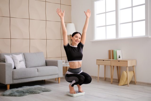 happy young woman checking her weight at home