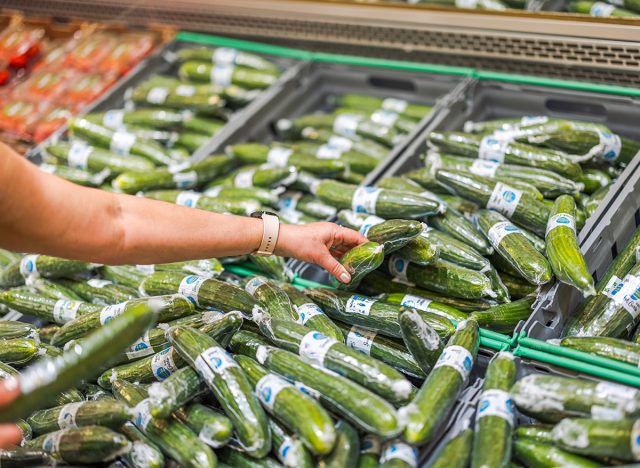 close-up view of a hand picking up a cucumber wrapped in vacuum packaging from the shelf in the store.